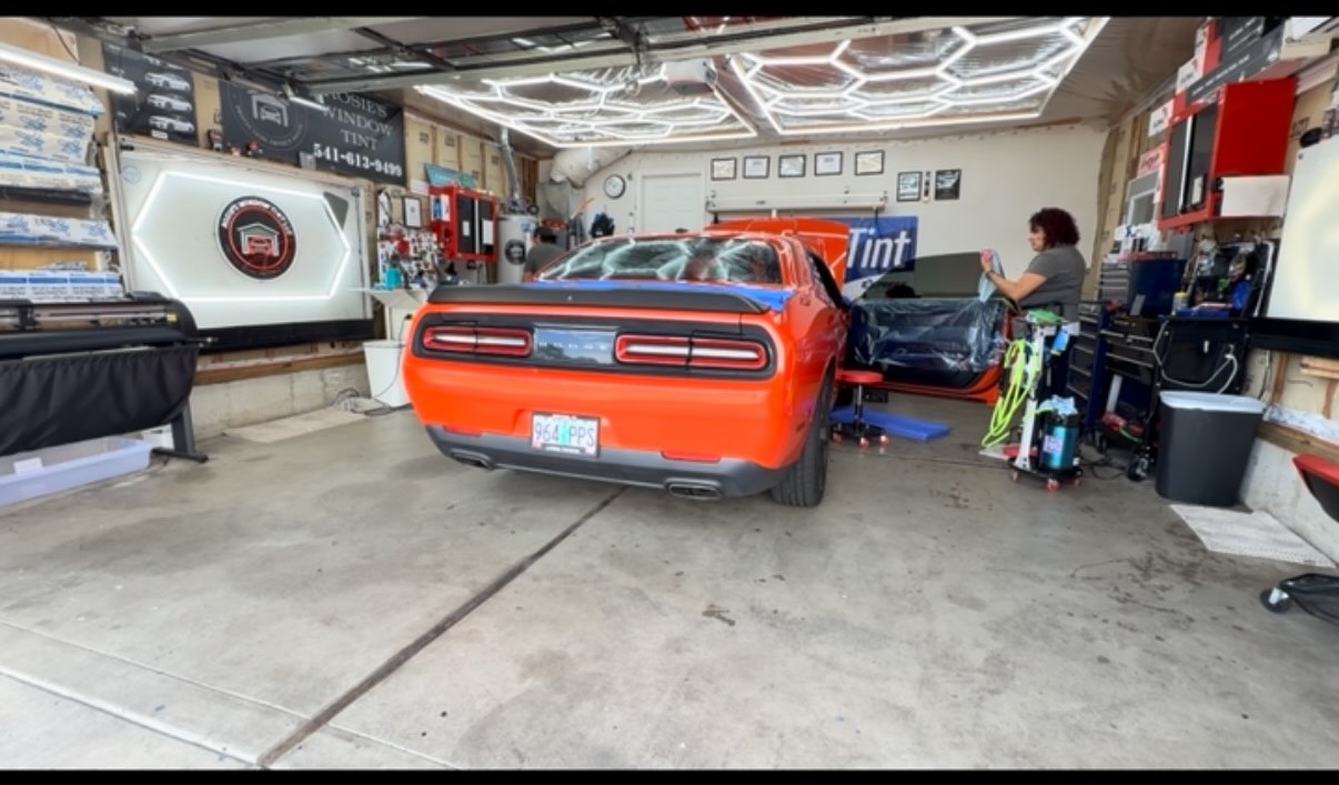 Orange Dodge Challenger being tinted inside Rosie's Window Tint studio under hex lighting