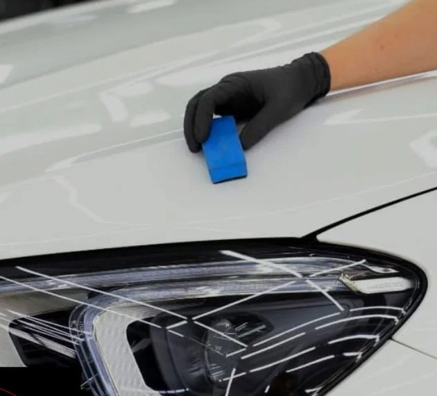 Gloved installer fitting paint protection film around a headlight and fender edge